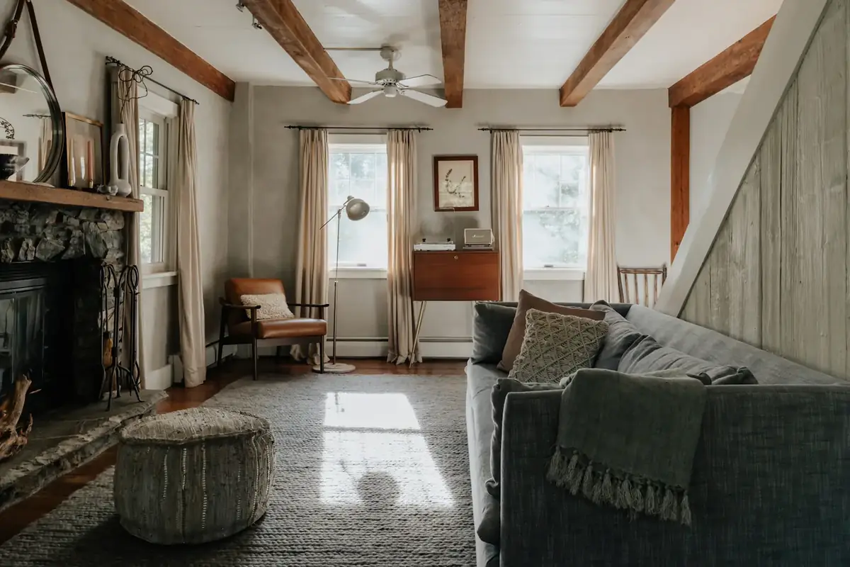 Finished great room with exposed beams, a stone fireplace and a linen sofa