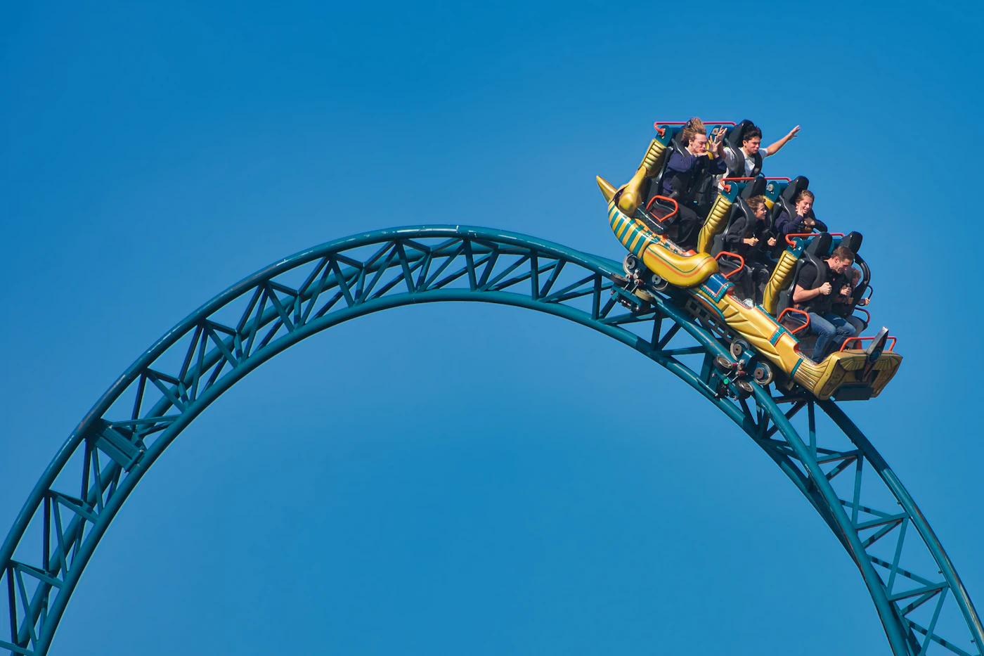 Riders cresting a roller coaster loop against a blue sky